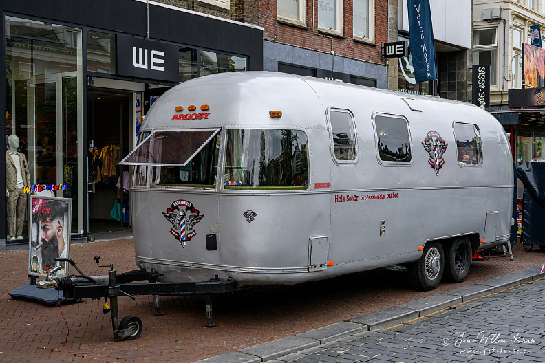 Old aluminium silver coloured caravan housing a mobile barber shop