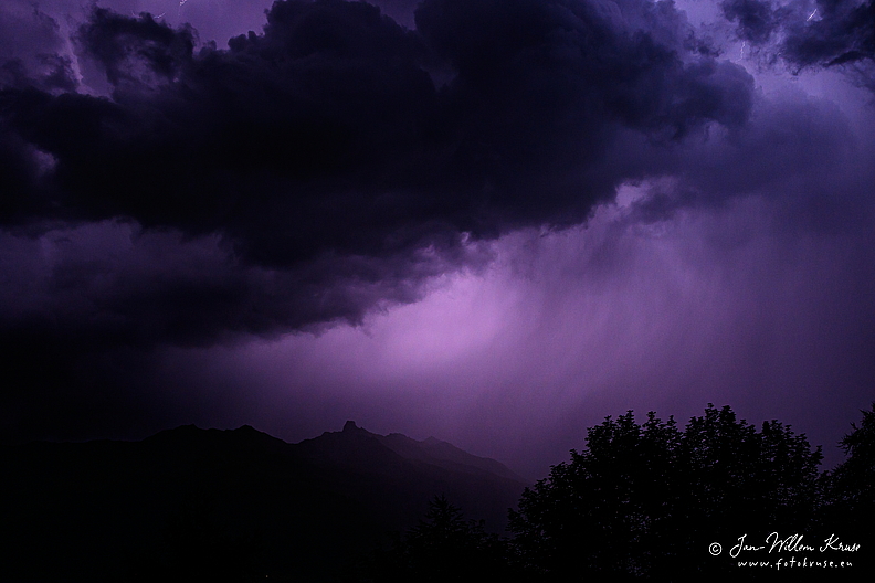 Thunderstorm in the night in Val d'Hérens creating the sky in purp-le against dark clouds