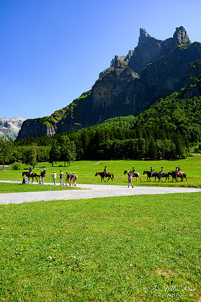 Mountain peak Corne du Chamois (Chamois Horns) rising high from the green meadow at Cirque du Fer à Cheval with horse riders in the foreground