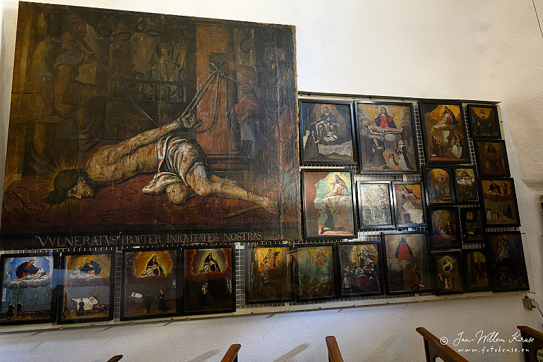 Wall densely covered with historic painted ex-votos around a large devotional image of Christ at Longeborgne.