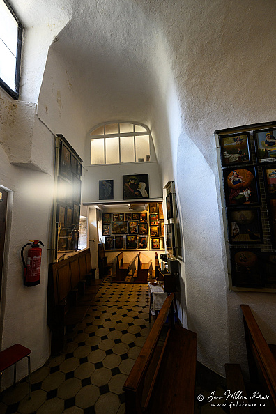 Narrow rock-ceilinged passage with benches and devotional images inside Longeborgne hermitage.