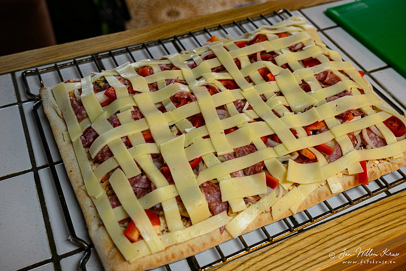 Unbaked rectangular pizza with a lattice of cheese strips over mixed toppings.