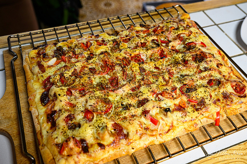 Freshly baked rectangular pizza with browned cheese and mixed vegetable and salami toppings.