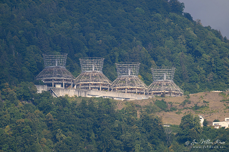 Four large skeletal cooling-tower structures on a forested Alpine slope.