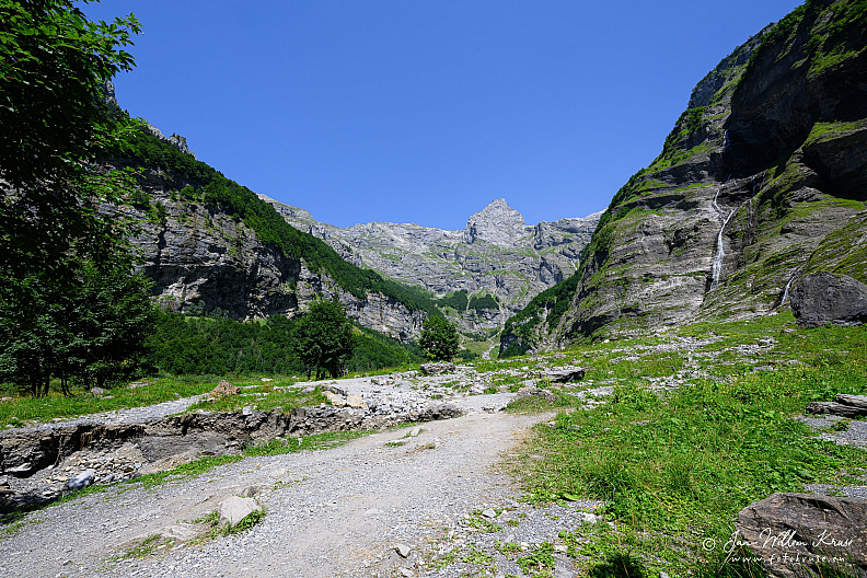 Gravel hiking trail and stony riverbed leading between towering limestone cliffs.