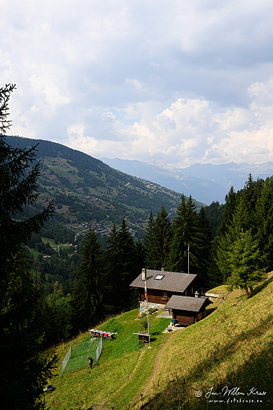 Single chalet on a steep grassy slope with forest and valley beyond.
