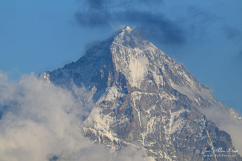 Sharp pale rock mountain summit emerging from dark blue-grey cloud.