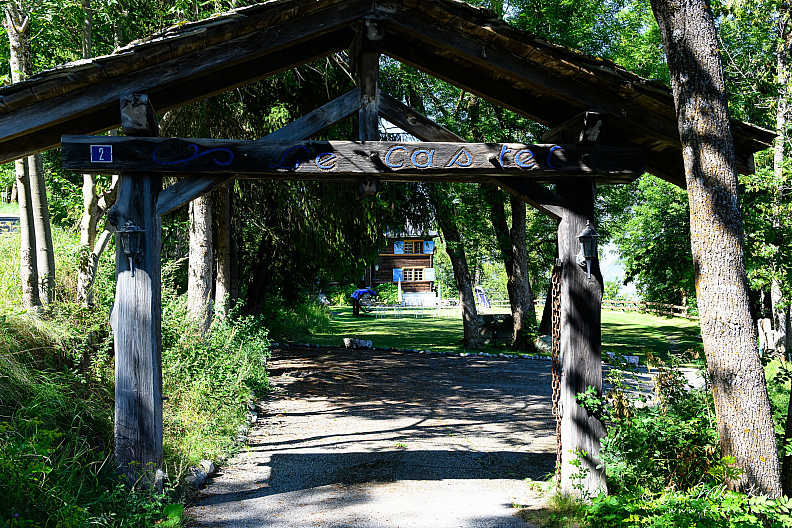 Heavy timber gateway with the name Le Castel and blue number 2 leading to a chalet garden.
