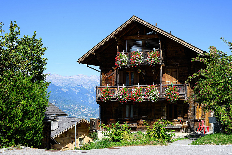 Traditional wooden chalet with balconies full of red and pink flowers.