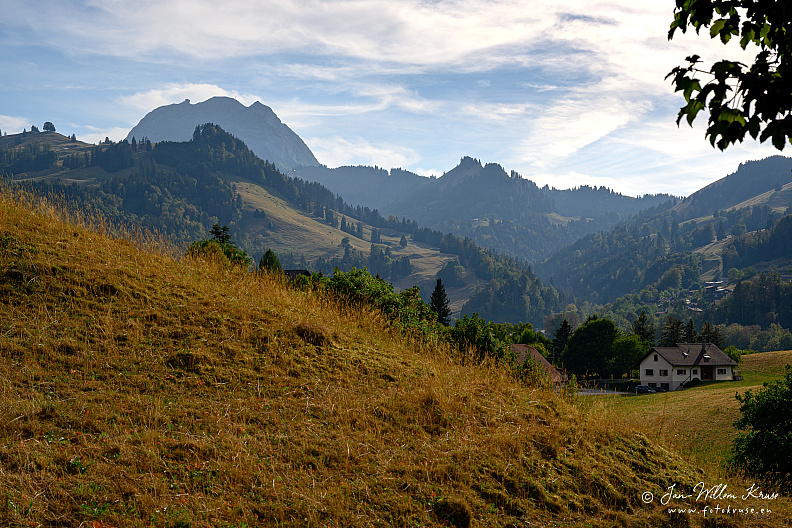 Dent de Broc and Dent du Chamois rising above sunlit grassland and houses near Gruyères.